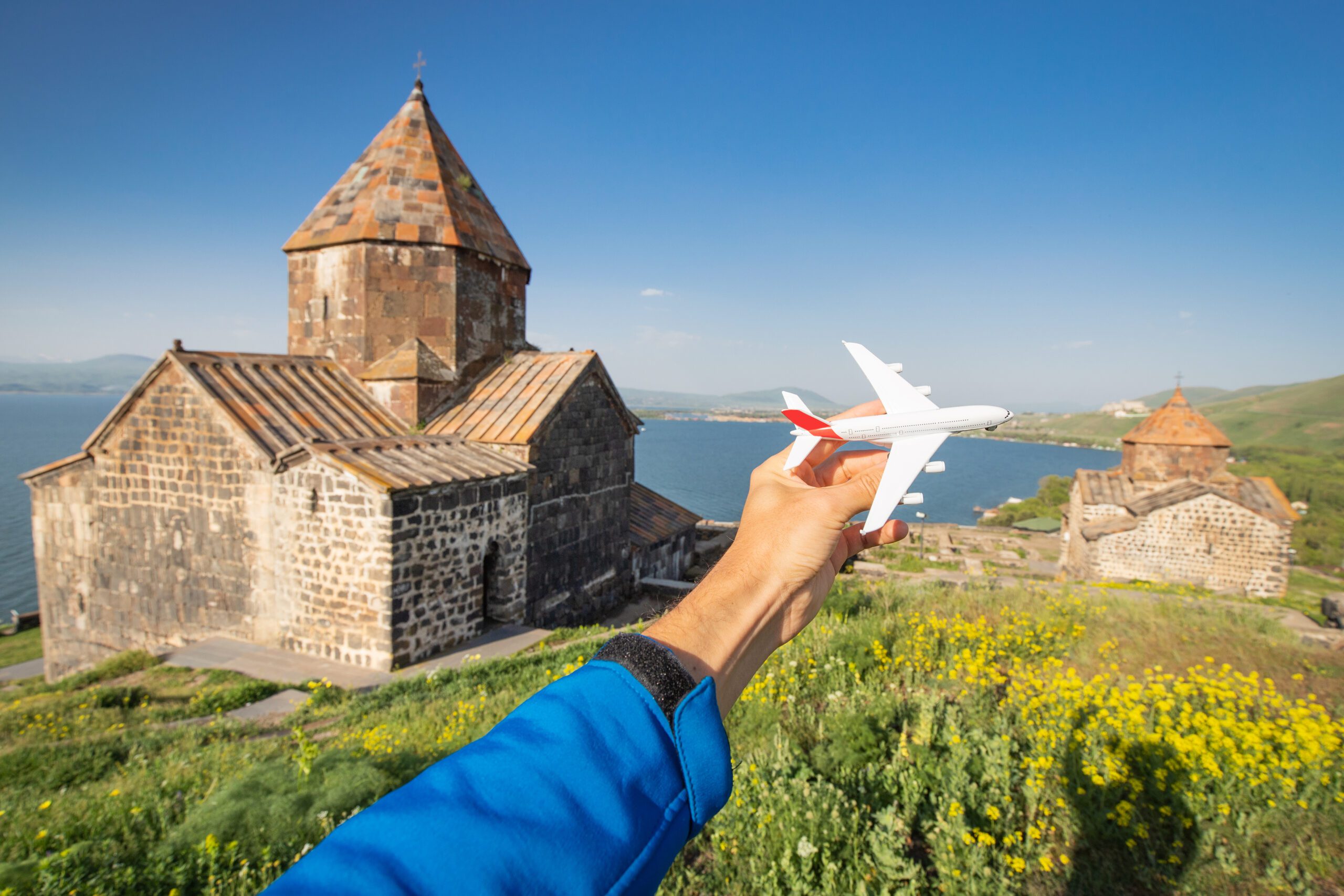 Tourist with a toy airplane on the background of a traditional Armenian ancient church and Sevan lake. Concept of air flight transportation