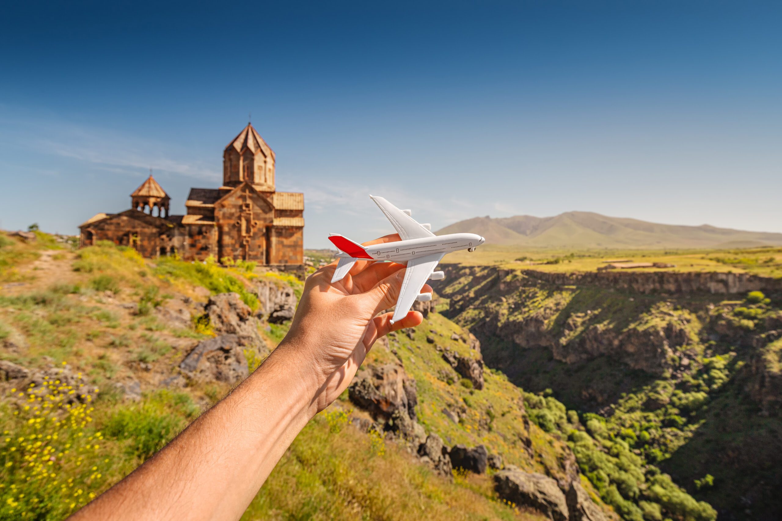 Traveler hand with a toy airplane on the background of a traditional Armenian ancient church. Concept of tourism and air flight transport