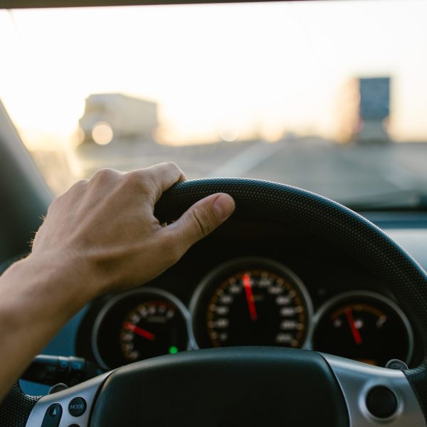 Selective focus man's hand on steering wheel, driving a car at sunset. Travel background.