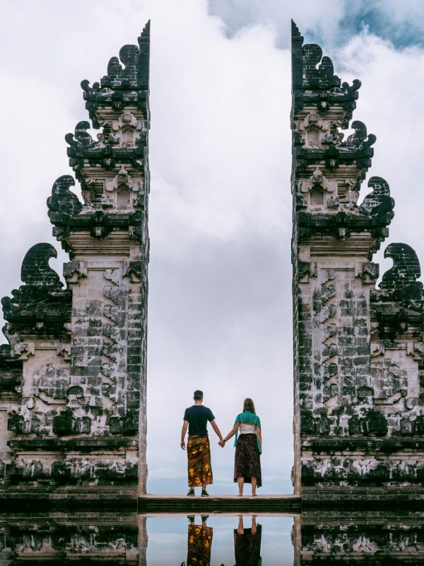Young couple standing in temple gates and holding hands of each other at Lempuyang Luhur temple in Bali, Indonesia. Vintage tone.